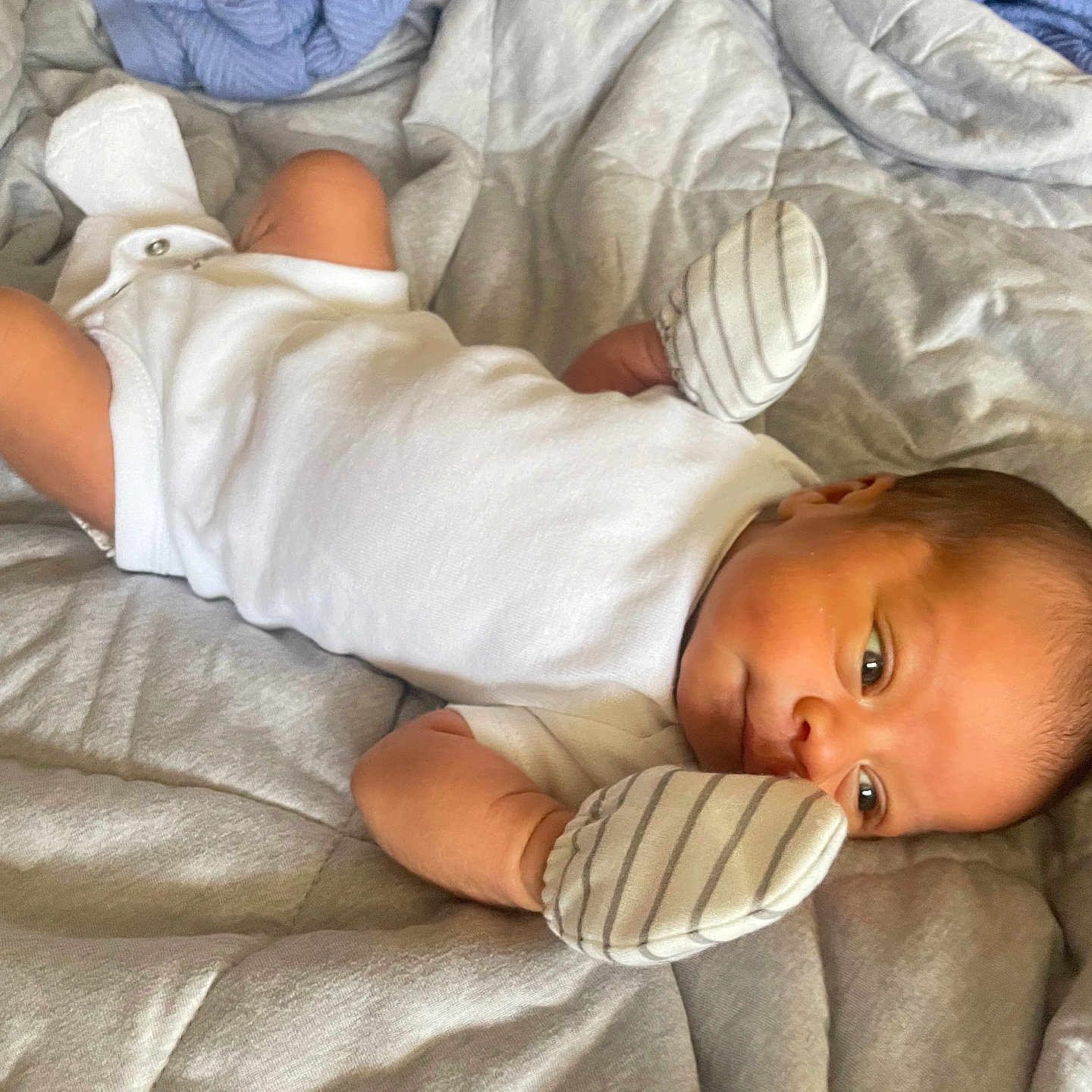 Feliciano joined the competition — help win amazing prizes! newborn, baby, infant, child, portrait, lying_down, bed, bedding, blanket, white_clothing, mittens, striped_mittens, wide_eyes, face, smiling, indoors, bedroom, cozy, photograph, closeup