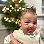 baby, child, face, tongue, mohawk, hand, clothing, holiday, christmas_tree, lights, indoor, person, smile, happy, infant, cute, portrait, blurred_background, warm_lighting, festive