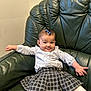 Eliana joined the competition — help win amazing prizes! baby, child, infant, smiling, blue_bow, plaid_skirt, white_tights, long_sleeve_shirt, green_leather_chair, indoor, cute, happy, relaxed, portrait, furniture, seated, person, skin, head, expression
