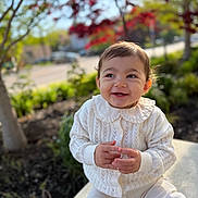Elena is registered to the contest to win money with this photo: toddler, child, smiling, white_sweater, outdoor, nature, greenery, red_leaves, sunlight, happy, cute, portrait, sitting, young_child, clothing, face, baby, daylight, trees, background_blur