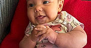 Haiti is registered to the contest to win money with this photo: baby, infant, smiling, hands, clothing, red_blanket, couch, indoor, cute, face, head, person, portrait, sitting, happy, expression, cozy, toddler, home, relaxing