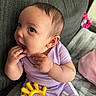 baby, infant, child, purple_clothing, teething_toy, hand, fingers, couch, blanket, indoor, face, head, sitting, cute, curious, toy, soft_texture, person, skin, smiling