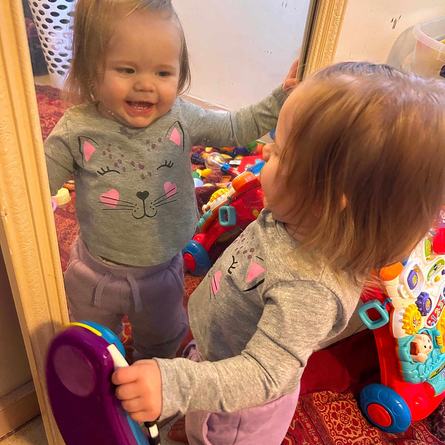 Lorelai Rain joined the competition — help win amazing prizes! barefoot, carpet, cat_face, child, furniture, gray_sweater, happy, home, indoor, laundry_basket, mirror, person, phone, playing, purple_pants, reflection, room, smiling, toddler, toy