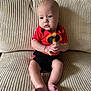 baby, infant, child, couch, furniture, clothing, onesie, red, black, skin, feet, hands, face, portrait, indoors, texture, sitting, cute, expression, young