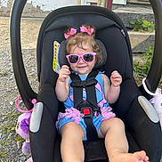 Natalie is registered to the contest to win money with this photo: baby, car_seat, child, clothing, cute, foot, grass, hair_bows, hand, happy, outdoor, person, pink, playful, rock, seatbelt, smile, summer, sunglasses, toddler
