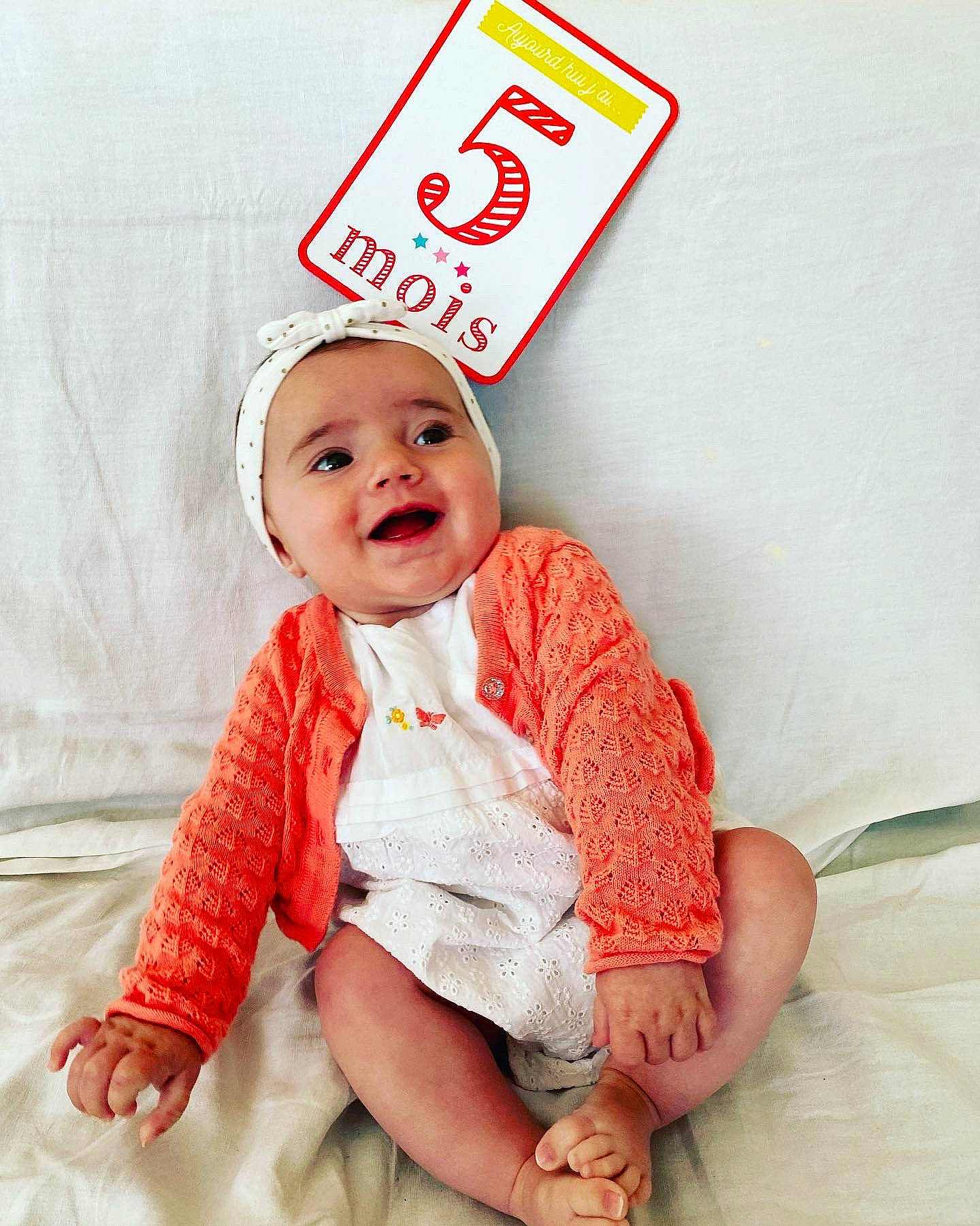 Juliette a rejoint le concours — aidez-le/la à gagner de superbes lots ! baby, baby_toddler_clothing, carmine, child, comfort, face, fashion_accessory, finger, font, fun, happy, headgear, headwear, linens, pattern, peach, person, sitting, sleeve, smile