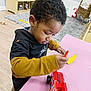 Kayden joined the competition — help win amazing prizes! toddler, child, toy_car, crayon, pink_table, yellow_banana_toy, playroom, rug, wicker_chair, wooden_floor, black_hoodie, mustard_sleeves, curly_hair, indoor, playing, concentration, furniture, wooden_shelf, floor_toys, casual_clothing
