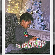Kayden is registered to the contest to win money with this photo: child, christmas_tree, holiday, pajamas, couch, indoors, decorations, lights, ornaments, technology, handheld_device, young_child, cozy, festive, seasonal, home, sitting, focused, celebration, winter