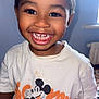 Kayden is registered to the contest to win money with this photo: child, toddler, smiling, face, teeth, mickey_mouse, tshirt, clothing, indoors, person, cute, happy, portrait, young_child, black_hair, short_hair, sitting, window, radiator, carpet