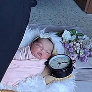 Aminah joined the competition — help win amazing prizes! baby, basket, swaddle, clock, flowers, headband, sleeping, fluffy, blanket, wooden_floor, decor, indoor, portrait, infant, peaceful, soft, pink, white, purple, cozy