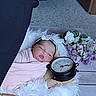 baby, basket, swaddle, clock, flowers, headband, sleeping, fluffy, blanket, wooden_floor, decor, indoor, portrait, infant, peaceful, soft, pink, white, purple, cozy