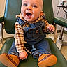 baby, child, smile, happy, denim_overalls, plaid_shirt, brown_shoes, green_chair, indoor, person, cute, infant, sitting, clothing, footwear, expression, young_child, portrait, room, joyful