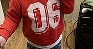 Messiah is registered to the contest to win money with this photo: toddler, child, curly_hair, red_sweatshirt, jeans, red_shoes, indoor, wooden_floor, person, standing, casual_clothing, thoughtful, hand_to_mouth, young_child, curly_curls, home, flooring, sweatshirt, footwear, portrait