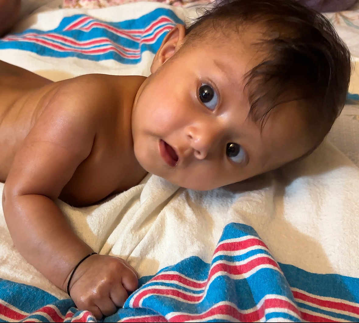 Luna is registered to the contest to win money with this photo: baby, infant, child, towel, striped_towel, skin, arm, hand, face, eyes, hair, indoors, lying_down, expression, curious, closeup, portrait, cute, newborn, soft_light