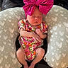 newborn, baby, sleeping, pink_bow, floral_onesie, baby_pillow, heart_pattern, couch, blanket, indoor, infant, clothing, resting, cute, small_baby, relaxing, person, headwear, soft_fabric, cozy
