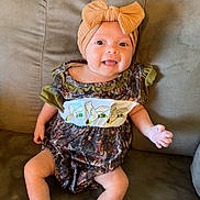Anslee joined the competition — help win amazing prizes! baby, child, infant, smiling, tongue_out, portrait, sitting, couch, sofa, bow_headband, headband, dress, floral_pattern, baby_clothing, indoors, home, furniture, barefoot, happy, photography