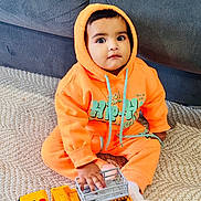 Erika joined the competition — help win amazing prizes! toddler, child, orange_hoodie, toy_truck, carpet, sitting, indoor, play, cute, cozy, furniture, person, clothing, expression, curious, small_toy, feet, hand, couch, casual