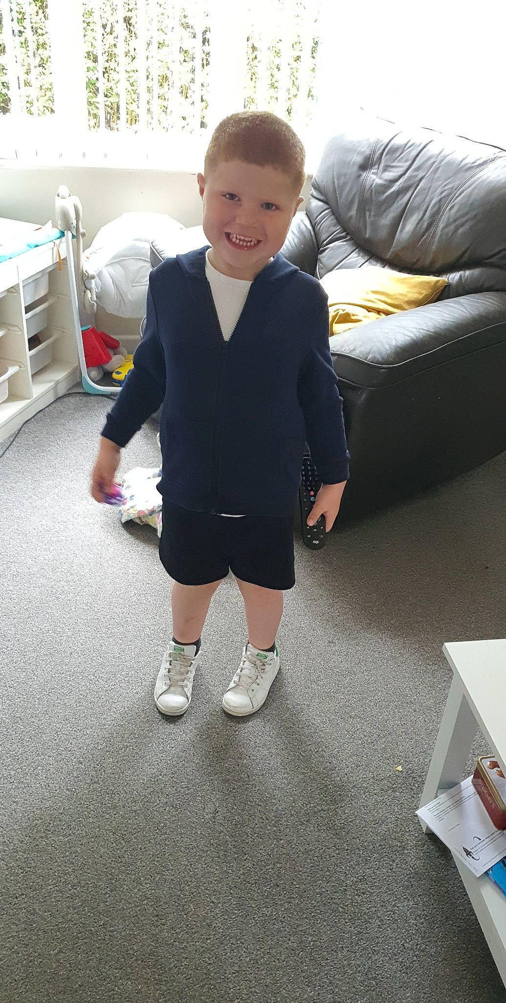 Tommie is registered to the contest to win money with this photo: child, comfort, couch, eye, face, flooring, fun, human_leg, joy, knee, leg, person, shorts, sleeve, smile, sneakers, sock, sportswear, t_shirt, thigh