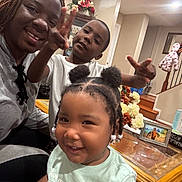 Arianna is registered to the contest to win money with this photo: woman, child, smiling, indoor, family, living_room, staircase, flowers, table, framed_photo, casual_clothing, portrait, happy, people, home_decor, braided_hair, playful, furniture, beads, gesture