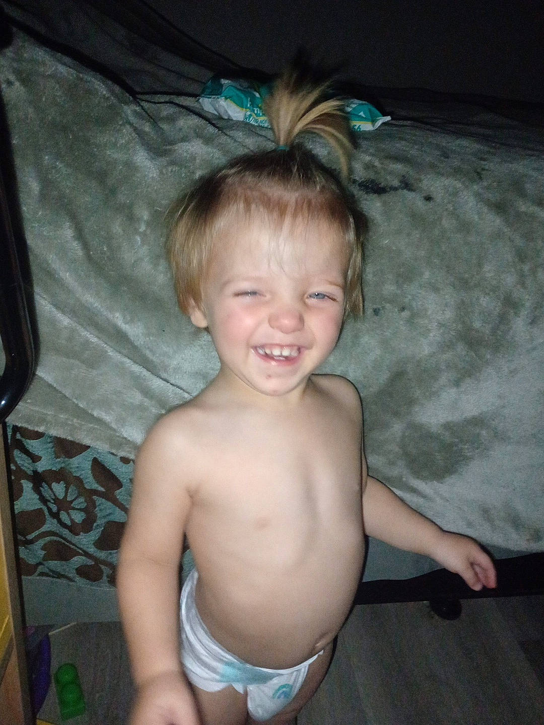 Colt is registered to the contest to win money with this photo: bare_torso, bed, blanket, carpet, child, diaper, face, flash, floor, furniture, hair, happy, indoor, laughing, person, pillow, ponytail, smiling, toddler, toy