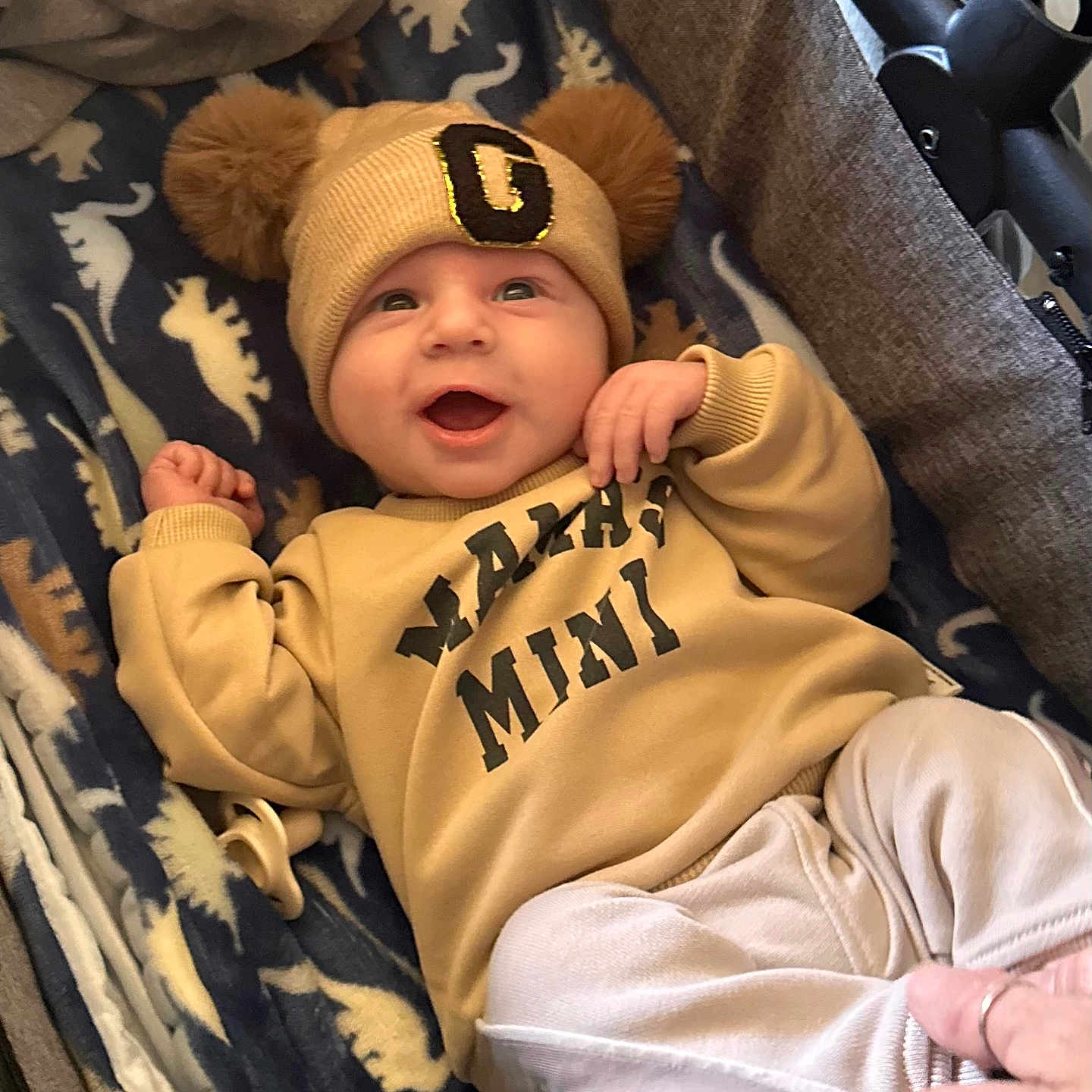 Graysyn joined the competition — help win amazing prizes! baby, blanket, child, clothing, cozy, cute, dinosaur_pattern, hand, happy, hat, indoor, infant, lying_down, newborn, person, pom_poms, portrait, smiling, sweatshirt, warm_clothing