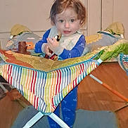 Silas is registered to the contest to win money with this photo: toddler, child, indoor, playpen, toy, pajamas, baby, floor, door, wood, colorful, striped, fabric, standing, smiling, curly_hair, person, home, infant, young_child