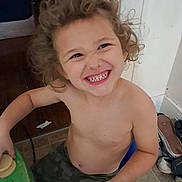 Luka is registered to the contest to win money with this photo: bare_chest, blue_chair, casual, child, curly_hair, floor_tiles, fun, green_table, happy, home, indoor, light_skin, person, playful, seated, shirtless, shoes, smiling, tooth_grin, young_child