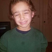 Martin Jr is registered to the contest to win money with this photo: child, smile, indoor, green_sweatshirt, curly_hair, face, person, portrait, young, happy, casual_clothing, wall, door, room, sweatshirt, childhood, kid, home, expression, squinting