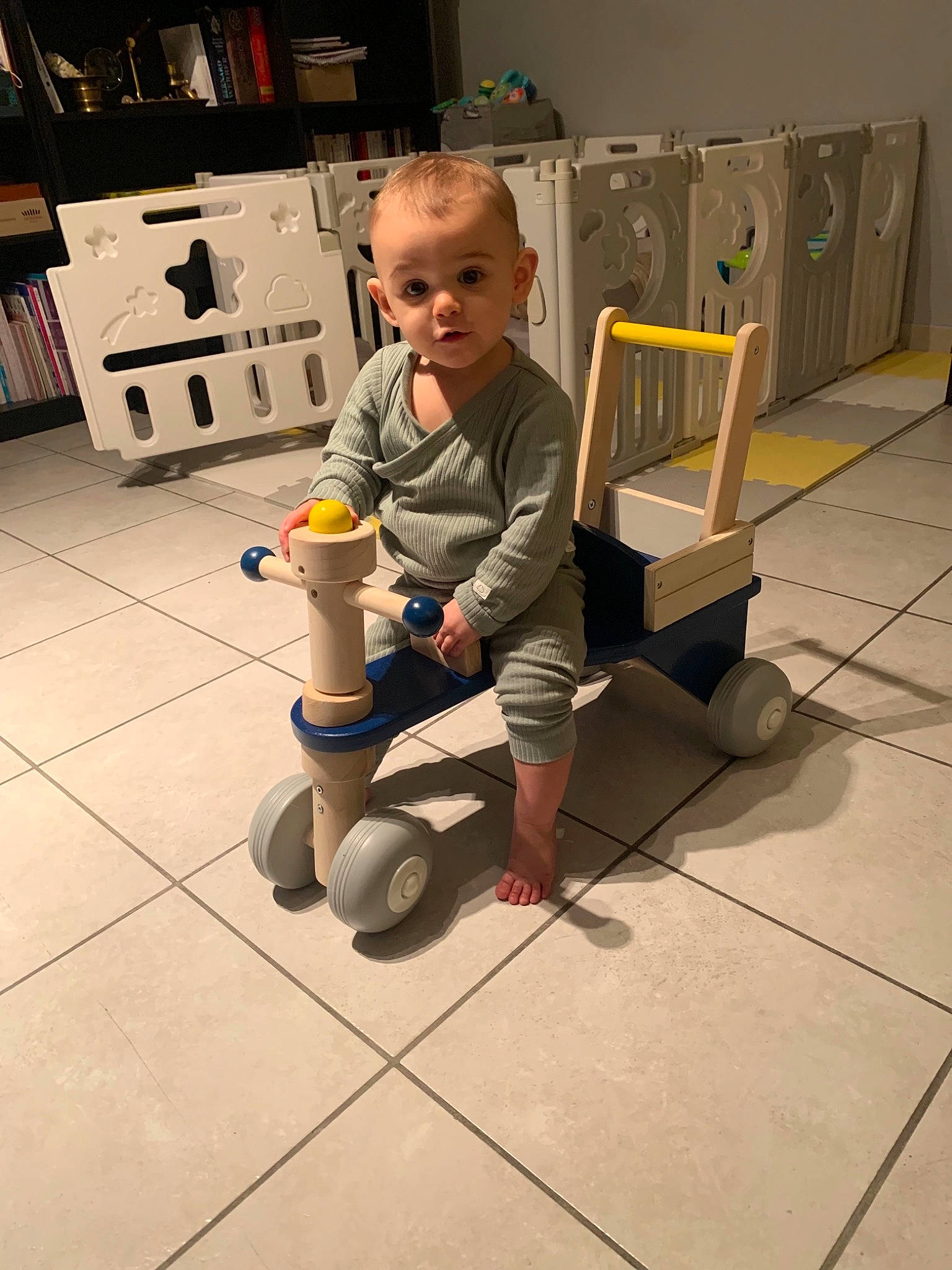 Erine participe au concours pour gagner de l'argent avec cette photo : baby, baby_products, bookcase, child, floor, flooring, fun, hardwood, human_body, human_leg, person, play, refrigerator, room, shelf, shelving, sitting, surprise, toddler, toy