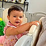 toddler, child, playpen, pink_dress, indoor, toy, shelf, framed_photos, curly_hair, earrings, smiling, handrail, soft_toys, baby, home, person, face, portrait, furniture, blanket