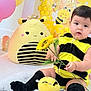 Alice is registered to the contest to win money with this photo: baby, child, costume, bumblebee, plush_toy, sunflower, flower, decorations, yellow, black, cute, infant, sitting, indoors, soft_rug, toy, face, portrait, happy, playful