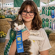 Ranger joined the competition — help win amazing prizes! girl, cat, glasses, ribbon, award, four_h, county_fair, tent, bunting, rosette, hay_bales, straw, portrait, smile, pet, pride, booth, flowers, hands, background_people