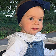 Sinaïe participe au concours pour gagner de l'argent avec cette photo : toddler, child, headband, bow, denim_overalls, white_shirt, earrings, outdoor, greenery, curious, portrait, baby, cute, face, hand, young_child, fashion, daylight, expression, playful