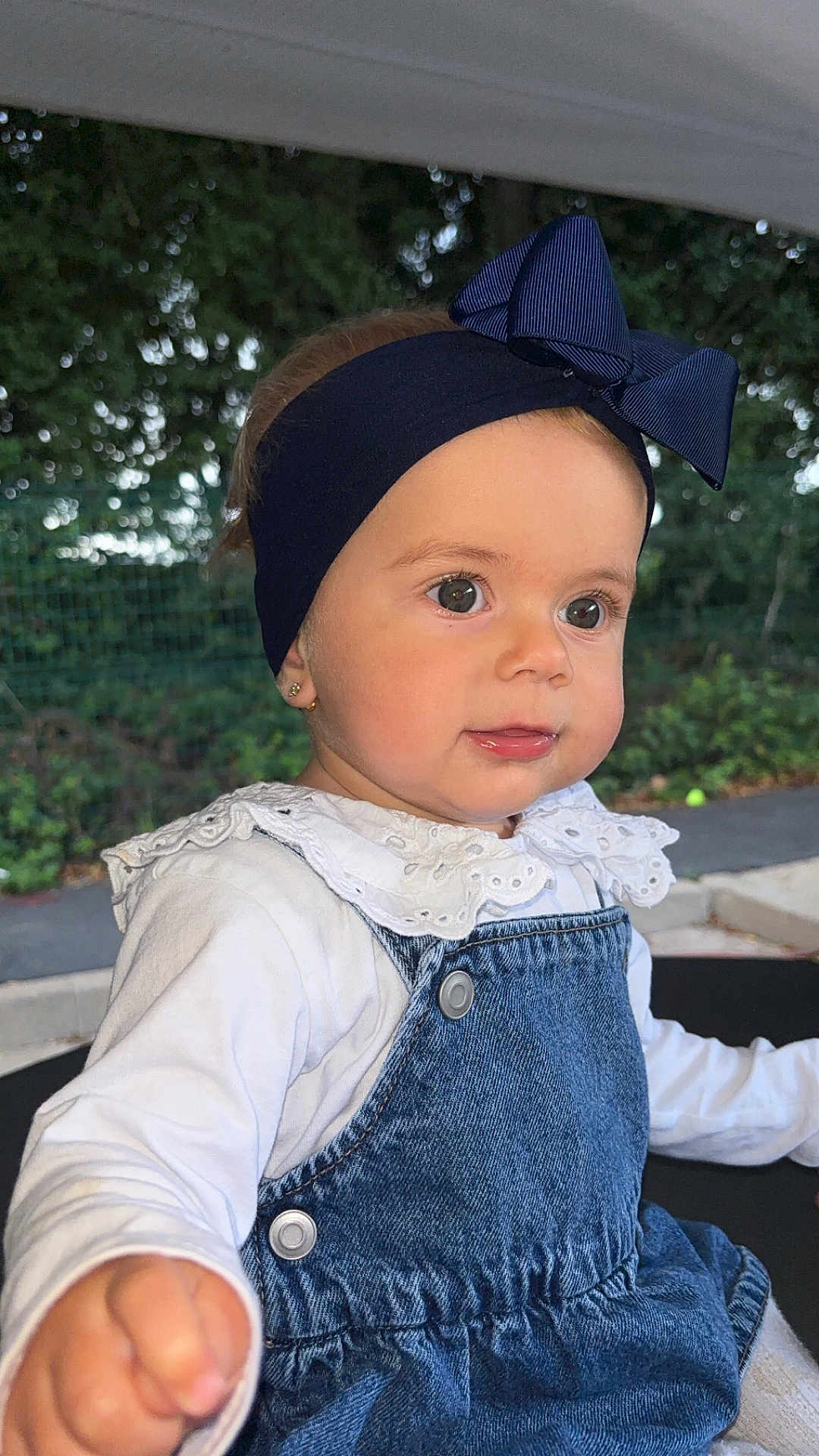 Sinaïe participe au concours pour gagner de l'argent avec cette photo : toddler, child, headband, bow, denim_overalls, white_shirt, earrings, outdoor, greenery, curious, portrait, baby, cute, face, hand, young_child, fashion, daylight, expression, playful