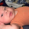 baby, infant, child, lying_down, portrait, face, eyes_open, wide_eyed, orange_outfit, striped_clothing, onesie, hand, arm, blanket, cushion, textile, indoor, cozy, home, photography