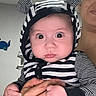 baby, child, infant, portrait, close_up, wide_eyed, zebra_outfit, striped_clothing, hat, indoors, adult, caregiver, holding, hands, family, home, seated, face, looking_at_camera, funny_expression