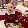 baby, child, toddler, maroon_outfit, teddy_bear_pattern, brown_shoes, white_rug, christmas_decorations, snowman, wrapped_presents, wooden_backdrop, festive, holiday, tinsel_garland, plush_pillow, red_decor, smiling, sitting, indoor, cute