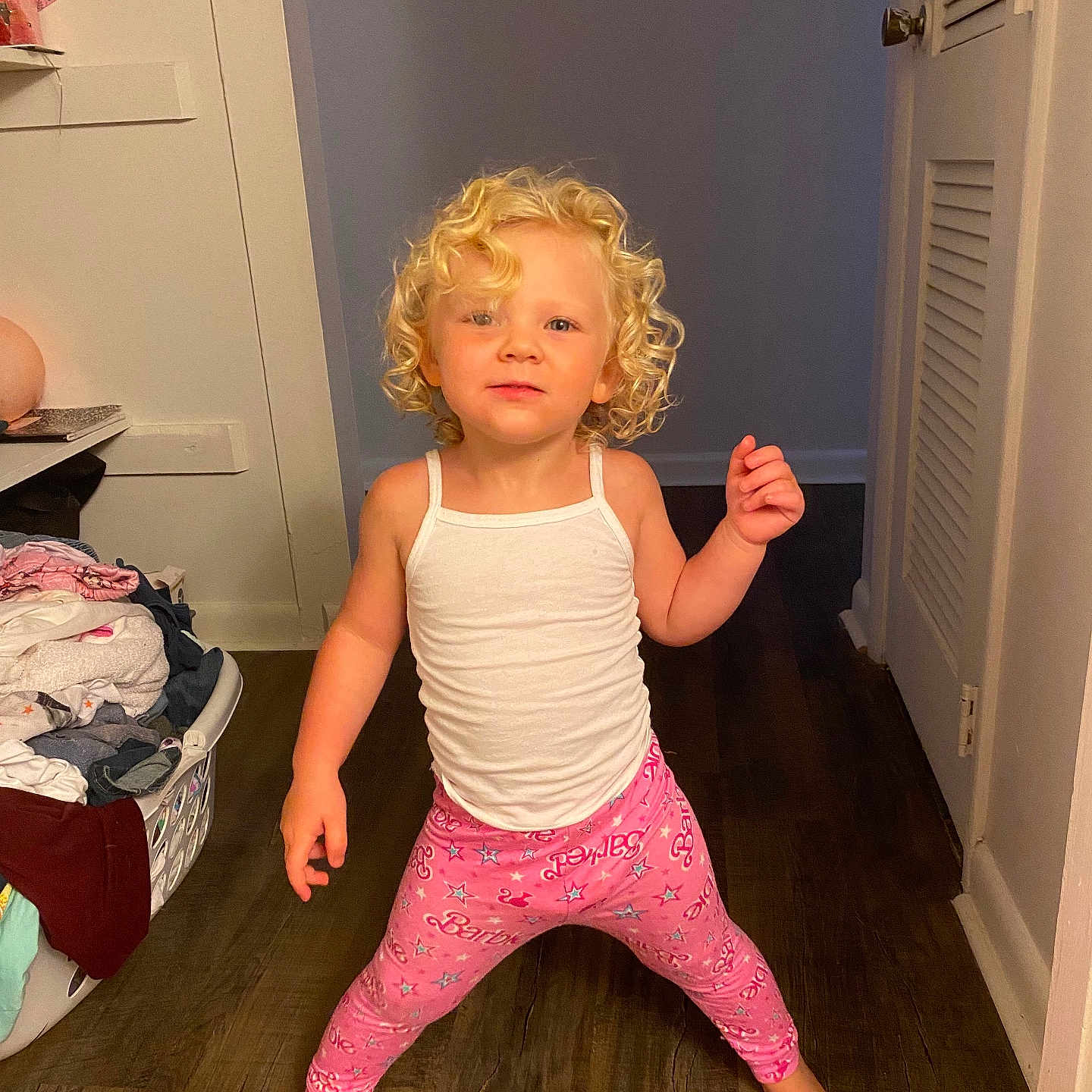 Ricki is registered to the contest to win money with this photo: child, toddler, curly_hair, blonde, tank_top, leggings, pink, barbie, standing, hallway, flooring, door, laundry_basket, clothes, barefoot, indoors, playful, pose, smile, person