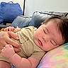 baby, sleeping, infant, hand, couch, pillow, tie_dye, colorful, peaceful, indoor, person, clothing, skin, face, resting, comfort, adult_hand, furniture, relaxation, closeup