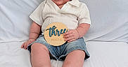 Leo joined the competition — help win amazing prizes! baby, bed, child, cute, denim_shorts, feet, hand, happy, indoors, infant, milestone, person, portrait, sitting, skin, smile, three_months, white_bedding, white_shirt, wooden_plaque