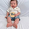 Leo joined the competition — help win amazing prizes! baby, infant, smile, white_shirt, denim_shorts, wooden_plaque, three_months, milestone, bed, white_bedding, cute, happy, sitting, indoors, portrait, child, person, skin, feet, hand