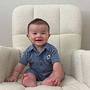 Leo is registered to the contest to win money with this photo: baby, child, smile, blue_clothing, armchair, indoor, infant, happy, cute, sitting, plush, soft_texture, foot, hand, portrait, person, young_child, light_wall, casual_clothing, short_hair