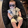 Leo joined the competition — help win amazing prizes! baby, sunglasses, baby_rocker, black, romper, infant, child, indoor, wooden_floor, footwear, straps, seat, comfort, relaxed, cute, person, casual_clothing, legs, hands, head