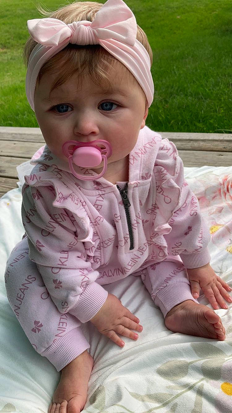 Alora is registered to the contest to win money with this photo: baby, baby_toddler_clothing, cheek, child, eye, finger, fun, grass, happy, head, lip, nose, person, pink, plant, product, recreation, sitting, skin, sleeve