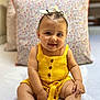 baby, child, smiling, yellow_outfit, sitting, pillow, indoor, cute, happy, face, person, clothing, footwear, infant, portrait, baby_girl, fashion, soft_lighting, closeup, headband