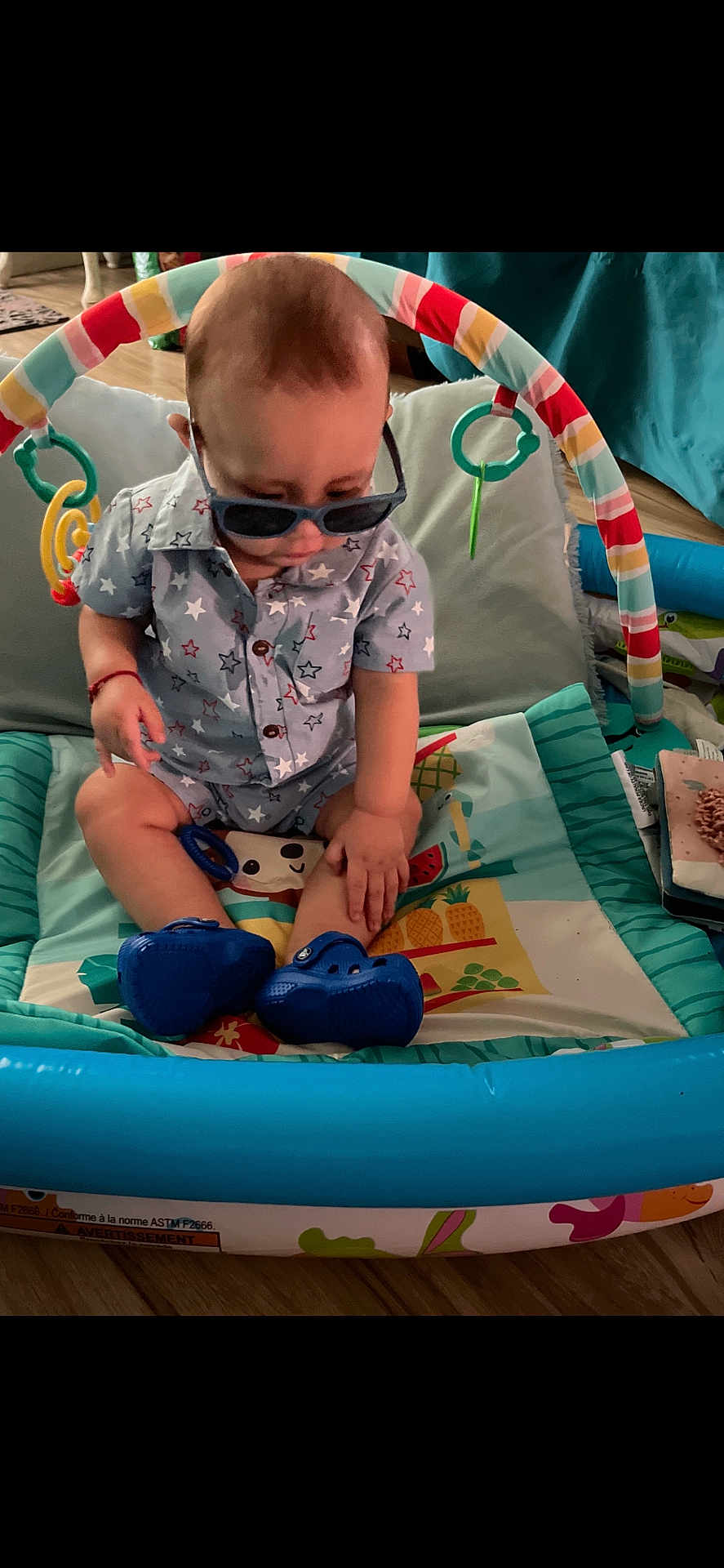 Aziel joined the competition — help win amazing prizes! baby, sunglasses, play_mat, toy, indoor, child, blue_shoes, shirt, star_pattern, floor, colorful, curious, seated, hand, head, face, clothing, footwear, baby_toys, playtime