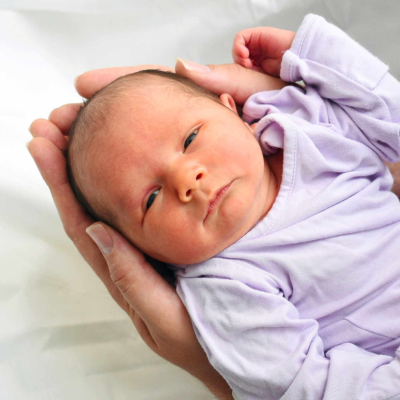Bonnie is registered to the contest to win money with this photo: newborn, baby, infant, hands, lavender_clothing, portrait, closeup, human, skin, face, peaceful, resting, soft, new_life, care, gentle, adult_hands, white_background, cute, sleepy