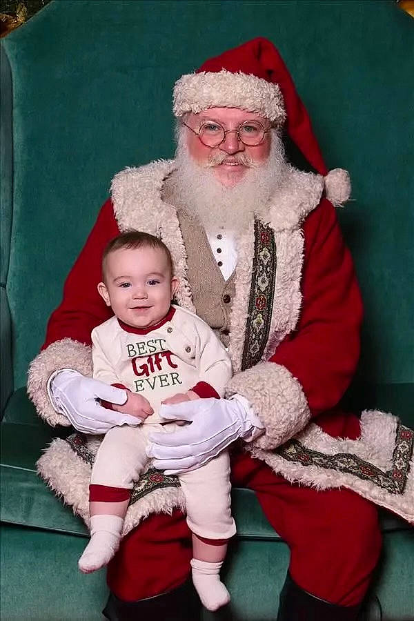 Lennox is registered to the contest to win money with this photo: baby, beard, child, christmas, christmas_eve, event, eye, facial_expression, fictional_character, happy, hat, head, headwear, holiday, human_body, joy, lap, person, red, santa_claus