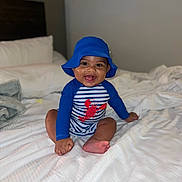 Julian joined the competition — help win amazing prizes! baby, bed, blue_hat, child, cute, foot, hand, happy, hat, headwear, indoor, infant, lobster_print, person, portrait, sitting, smiling, striped_clothing, swimsuit, white_bedspread