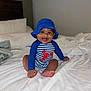 baby, bed, blue_hat, child, cute, foot, hand, happy, hat, headwear, indoor, infant, lobster_print, person, portrait, sitting, smiling, striped_clothing, swimsuit, white_bedspread